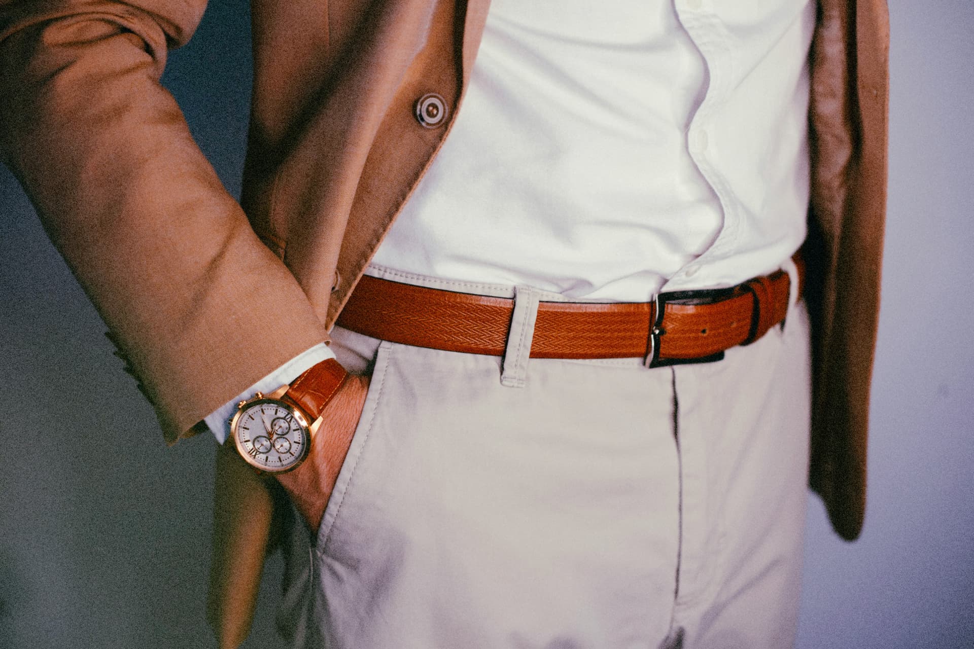 A man wearing a gold-toned watch with a tan blazer and braided belt
